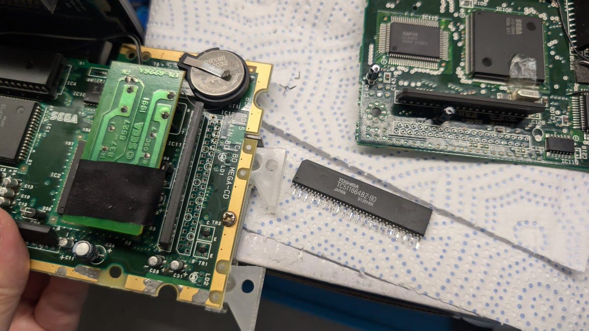 Extracted RAM package from donor MCD1 board held next to Wondermega motherboard during reinstallation troubleshooting.