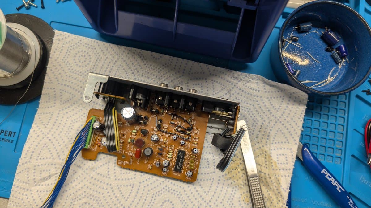 Victor RG-M1 AV board undergoing recap, capacitor leakage visible near regulators, soldering iron and desoldering tools on work mat.