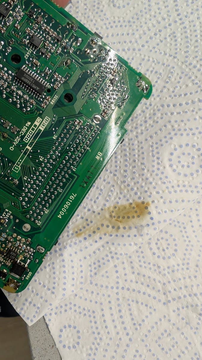 NEC PC Engine LT mainboard with heavy electrolyte corrosion near 5V regulator and power jack, cleaned residue visible on work surface.