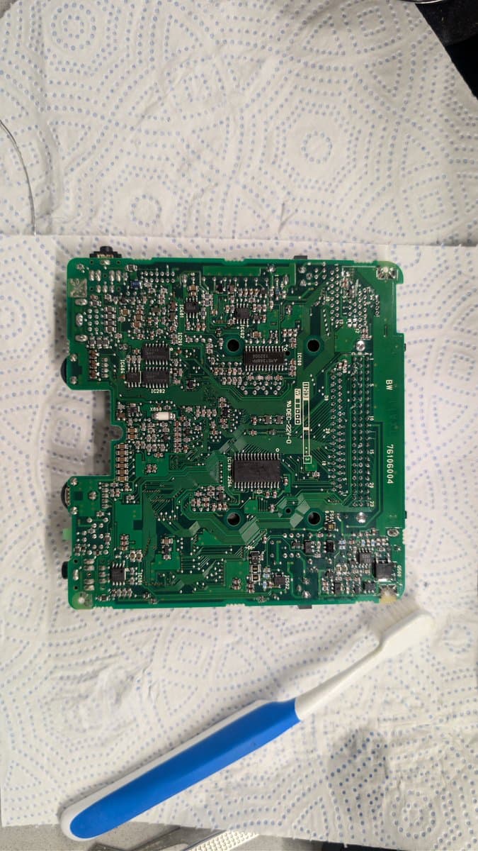 Cleaned NEC PC Engine LT circuit board displaying dense component layout, no visible trace damage; blue spudger tool beside board.