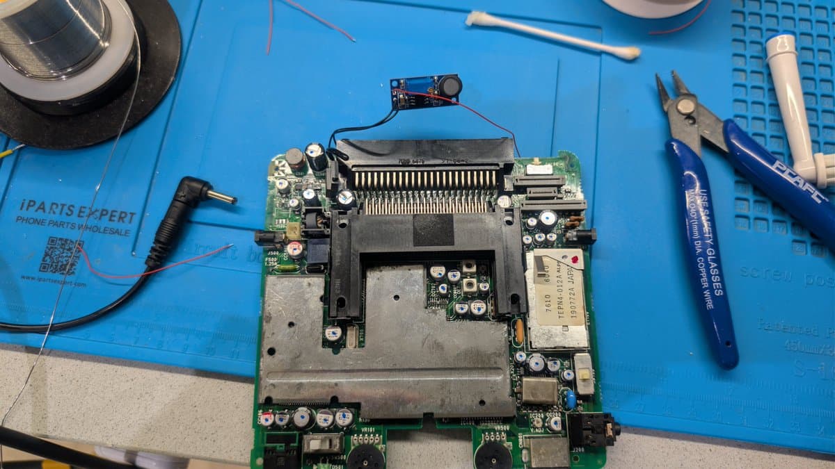 NEC PC Engine LT motherboard with replacement power module fitted into top shell recess, surrounded by repair tools on work mat.