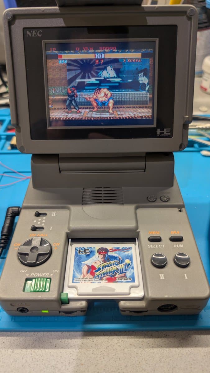 NEC PC Engine LT portable console displaying Street Fighter II in-game, with game card inserted in cartridge slot, showing successful repair completion.