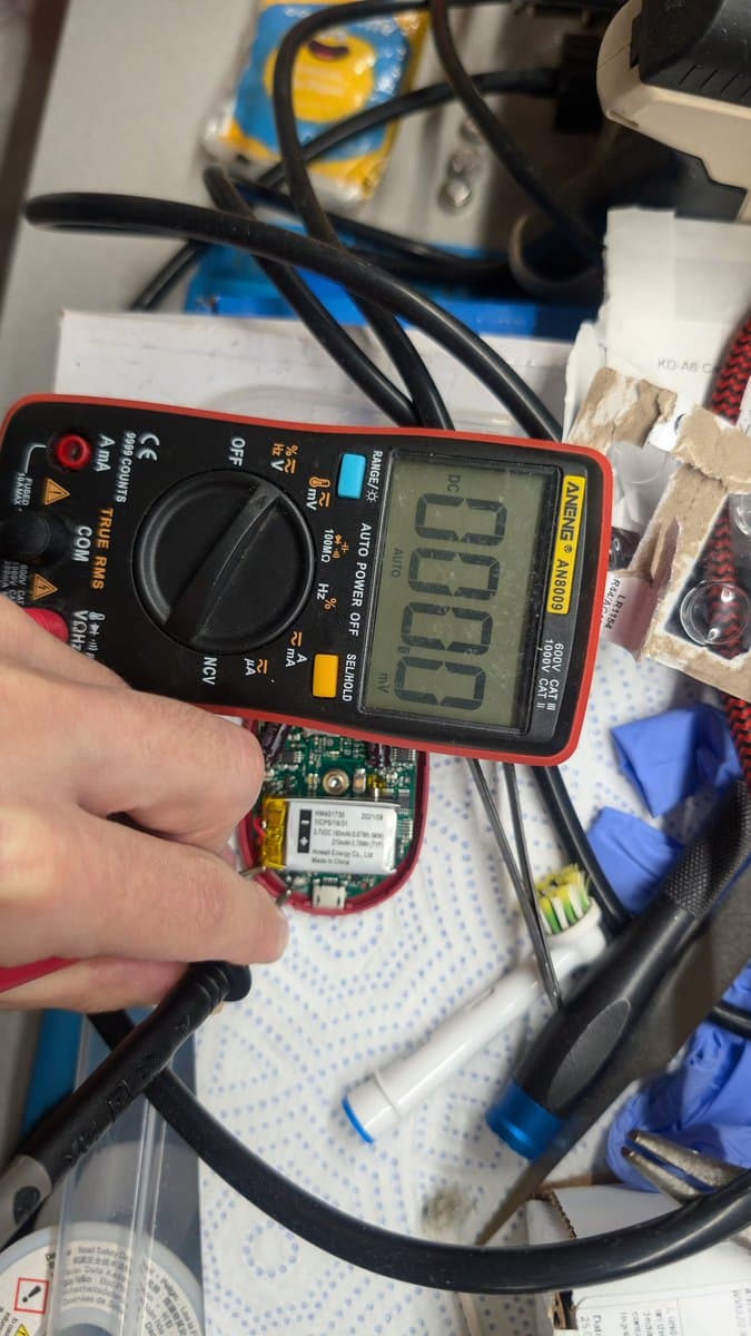 Digital multimeter displaying 0.00V reading on PowerDot PCB with desoldered USB port pins visible during repair diagnostics.