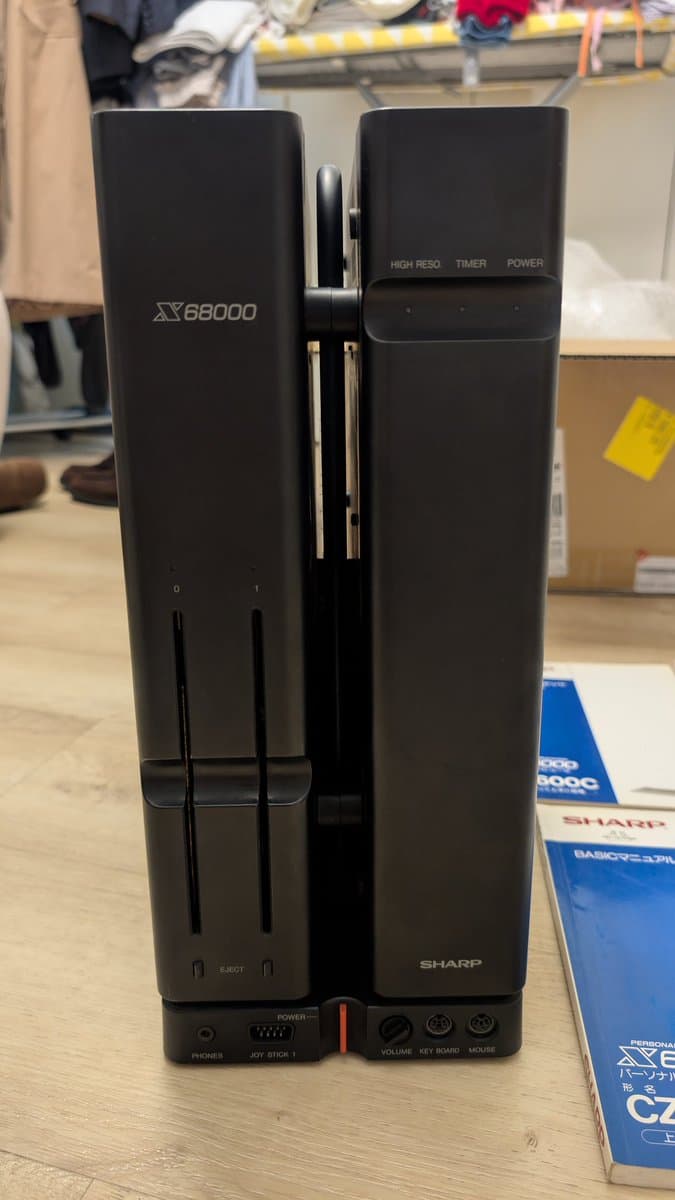 Sharp X68000 tower model displayed front-facing, showing X68000 branding, expansion slot, power button, and control panel with volume and joy stick inputs.