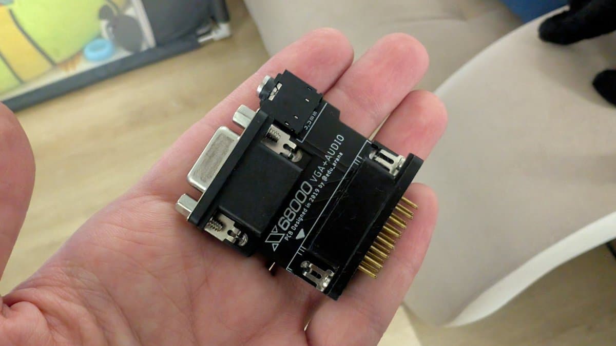 Sharp X68000 VGA adapter held in palm, showing D-sub connector, black housing with gold pin header, used for testing restored console output.