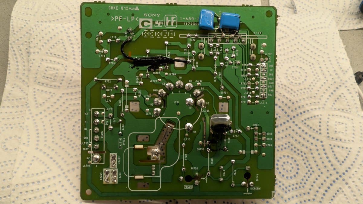 Sony PVM-14L1 neck board with reflowed solder joints, blue capacitors visible at top, components and traces throughout green PCB.