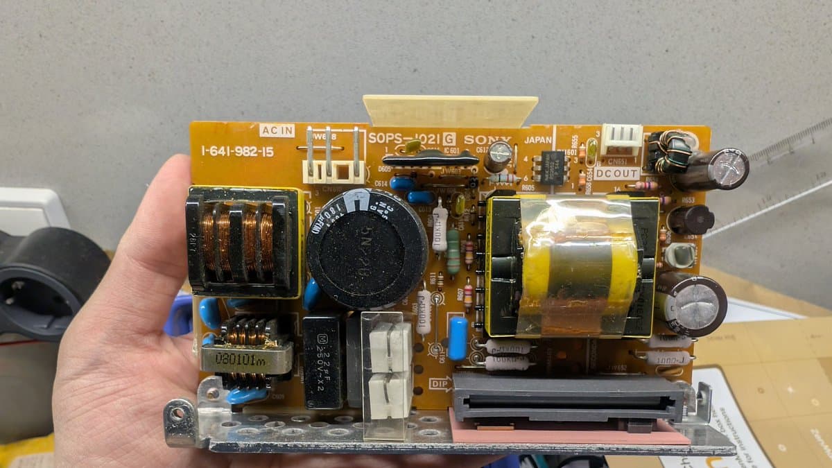 Sony PVM-6041Q power supply board held in hand, showing capacitors, transformer, and solder joints ready for restoration work.