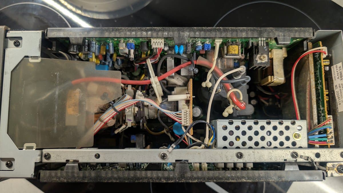 Interior of Sony PVM-6041Q with dusty PSU and circuitry visible. Red and black power wires, capacitors, transformers, and heat sinks shown before cleaning and refurbishment.