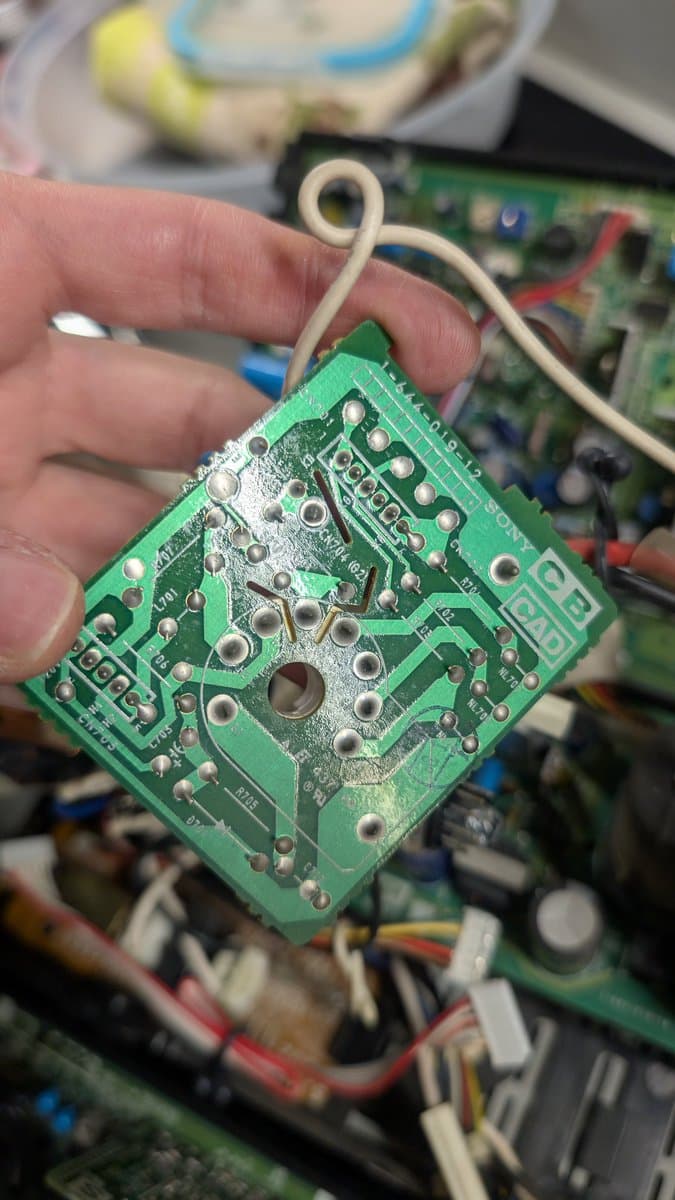 Closeup of small green neck board PCB held in hand, showing reflowed solder joints and single electrolytic capacitor replacement on Sony PVM-6041Q.