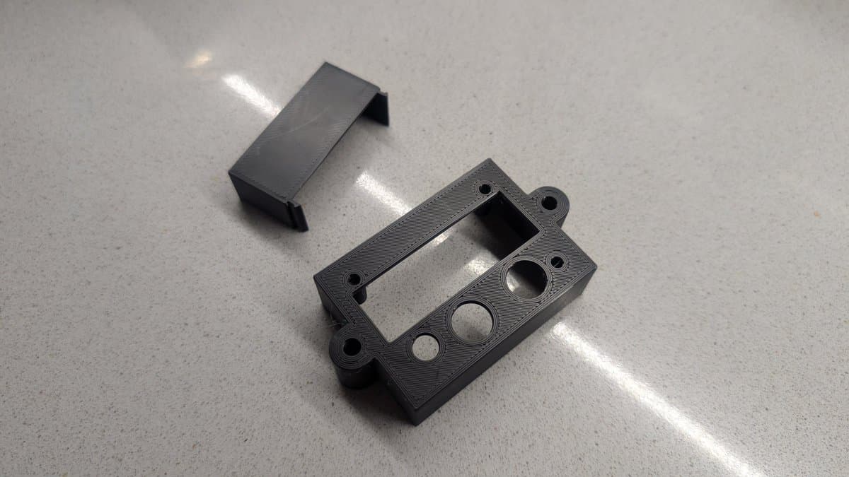 3D-printed black plastic shell components for PVM-14L1 RGB mod, showing rectangular cover and control panel with mounting holes and switch cutout.