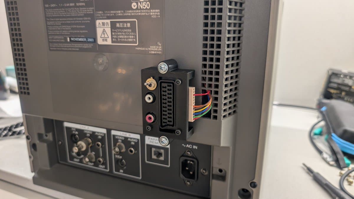 Custom RGB mod enclosure mounted on Sony PVM-14L1 rear panel, showing D-sub connector, audio toggle switches, and multicolored internal wiring.