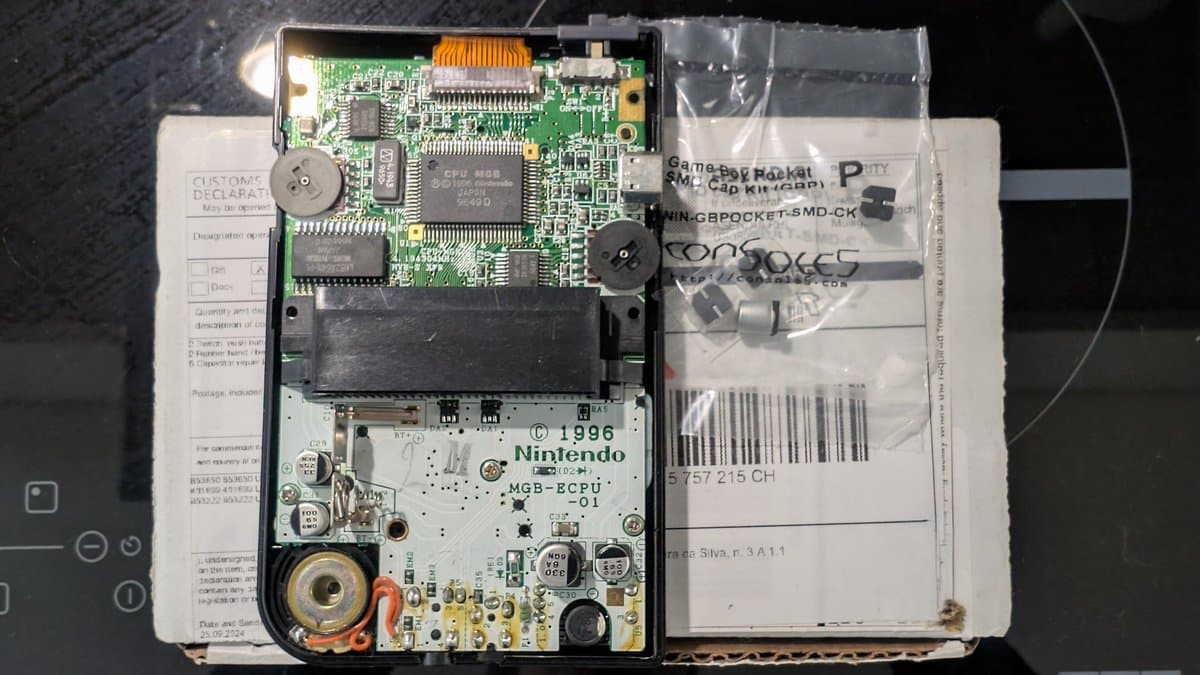 Game Boy Pocket motherboard opened showing CPU, RAM chips, capacitors, and power circuitry during restoration with documentation and replacement parts visible.