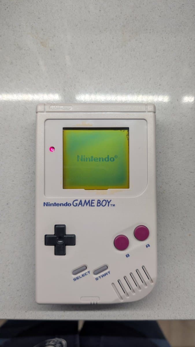 Nintendo Game Boy DMG with recapped motherboard, cleaned shell, working screen displaying Nintendo logo, magenta buttons, black d-pad visible.