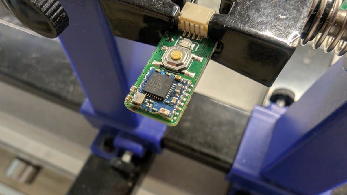 WavePhoenix PCB with freshly reflowed microcontroller IC centered on green board, surrounded by blue thermal clamps in rework vise.