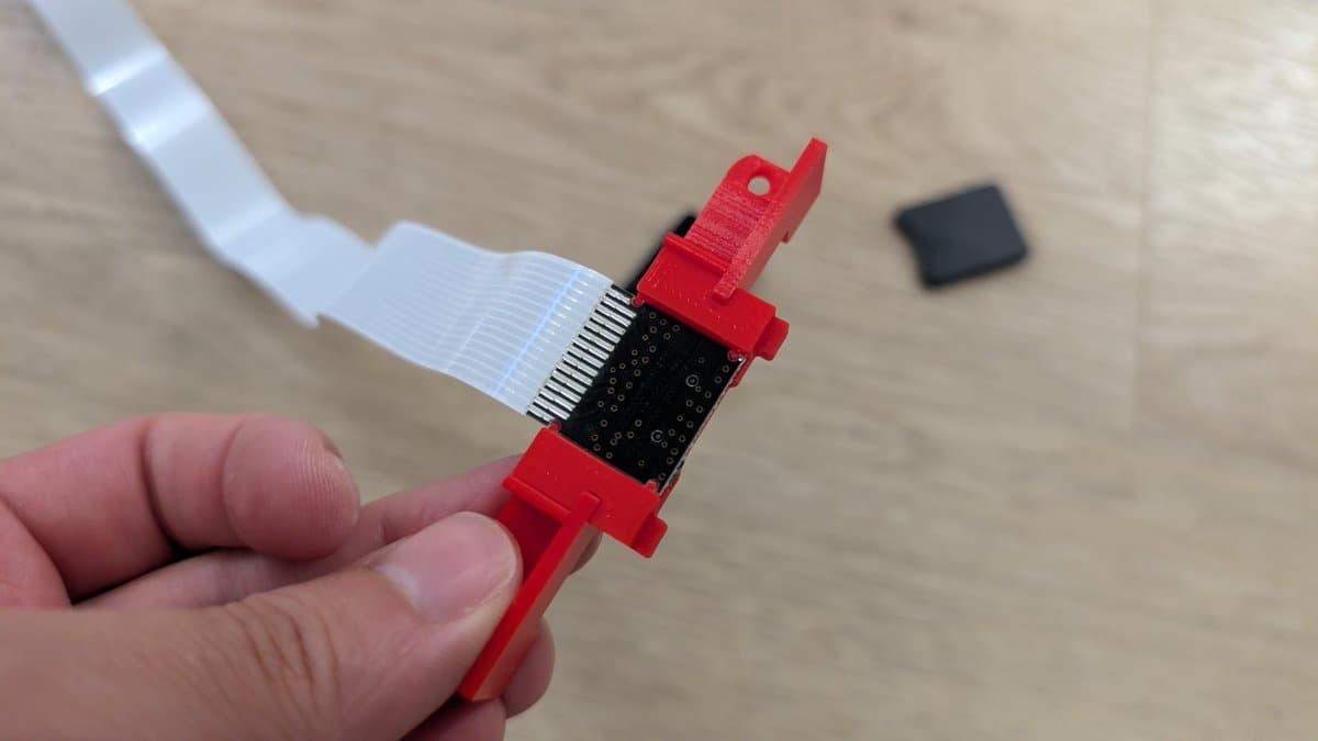 Red 3D-printed SD card extension bracket with flex cable connector attached, held in hand during 3DO ODE mod installation.