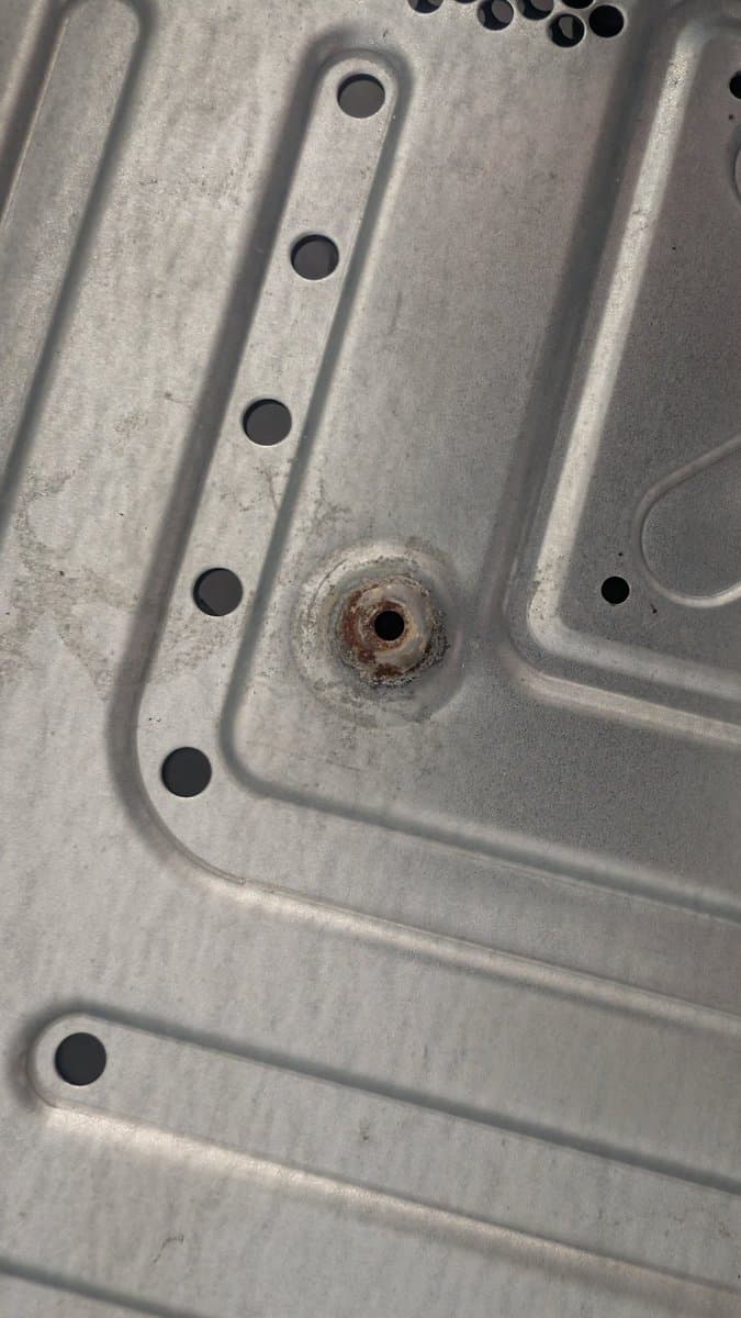 Rusted metal shield on Xbox 360 E motherboard with evaporust treatment applied; corrosion visible around fastener hole.