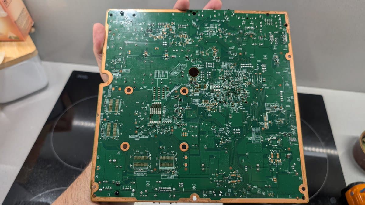 Xbox 360 E motherboard held in hand, freshly reflowed solder joints visible, board cleaned after oxidation removal and isopropyl alcohol wash.