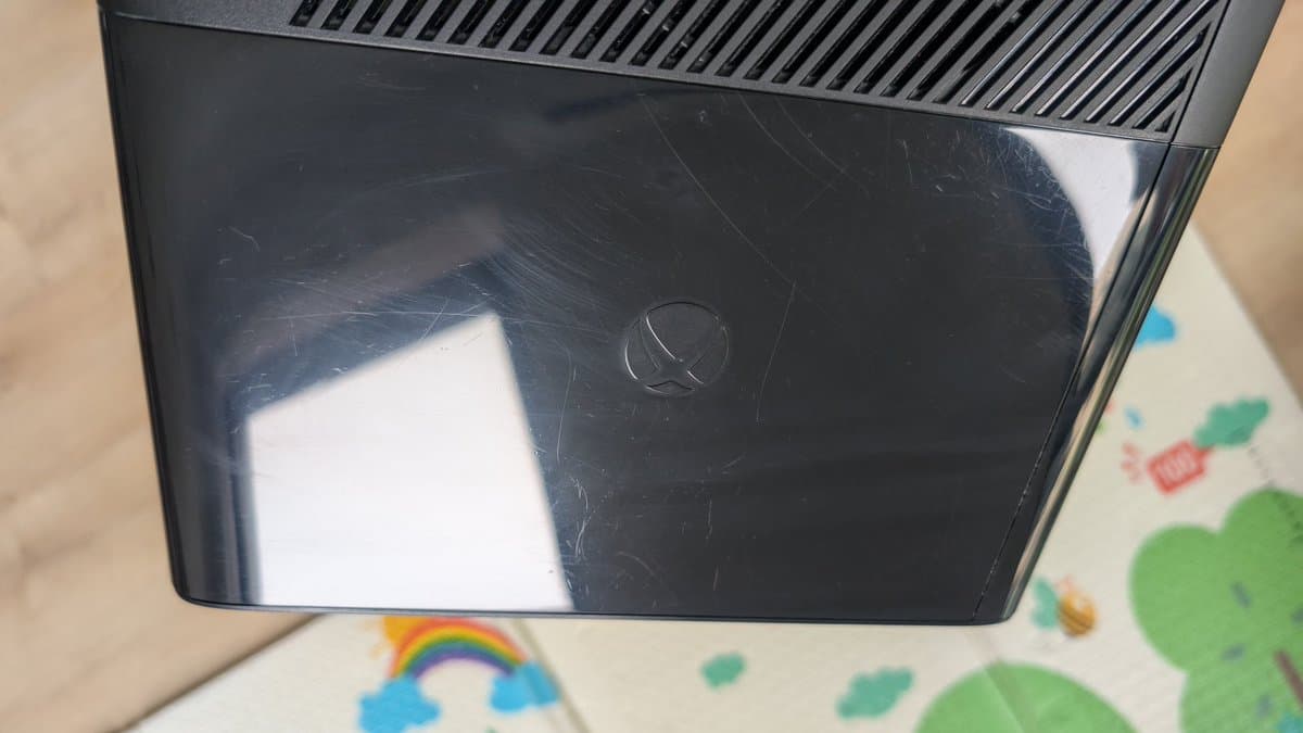 Xbox 360 E black plastic shell with visible scratches and scuffs, partially polished to reveal glossy finish after restoration work.