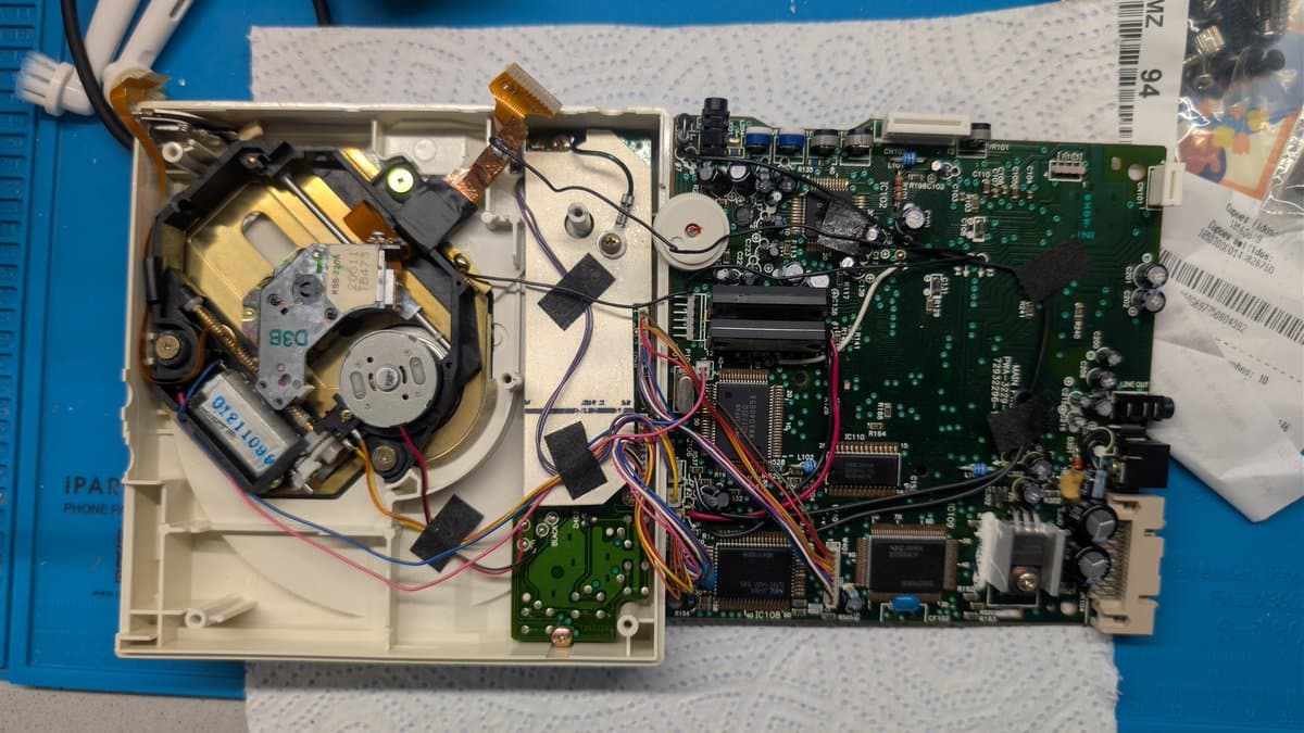 PC Engine CD-ROM2 internals: optical drive assembly on left, main logic board on right with visible capacitors, wiring, and IC chips during restoration work.