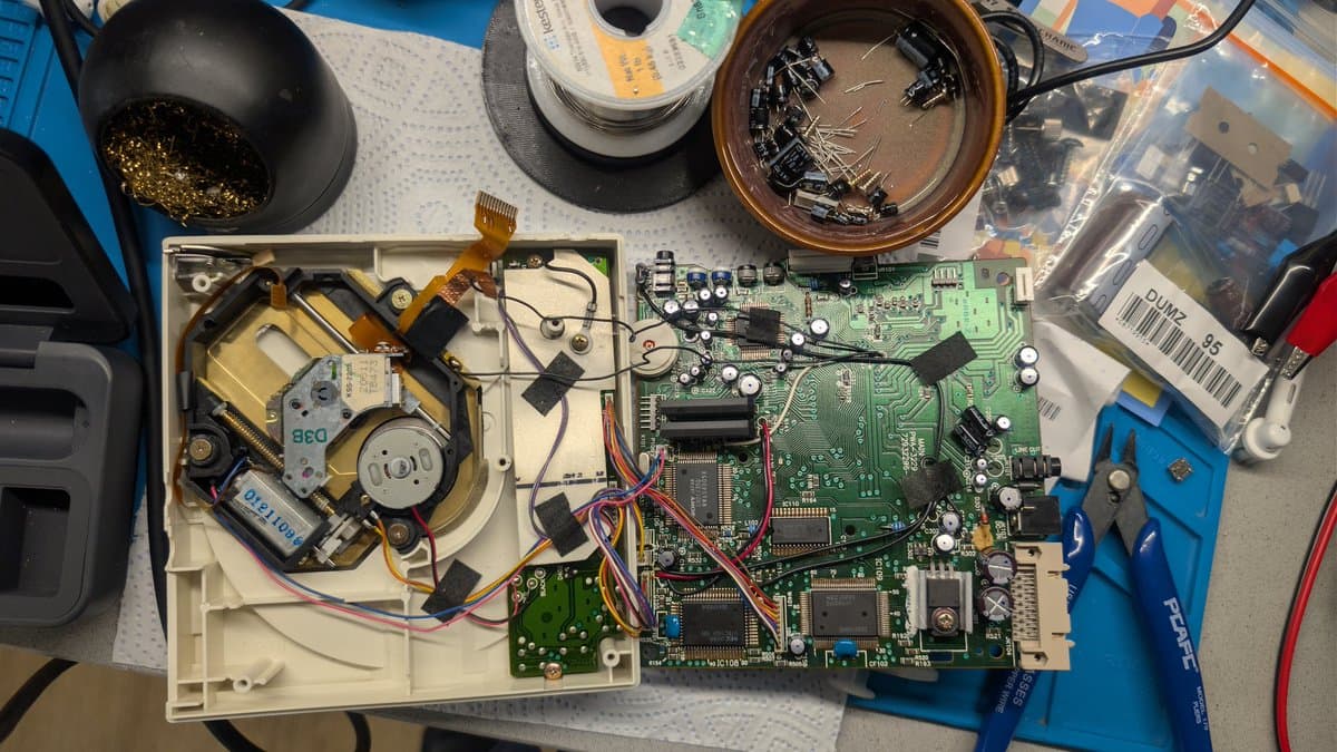 Disassembled PC Engine CD-ROM2 showing mainboard, laser assembly, motor components, and repair tools during restoration work.